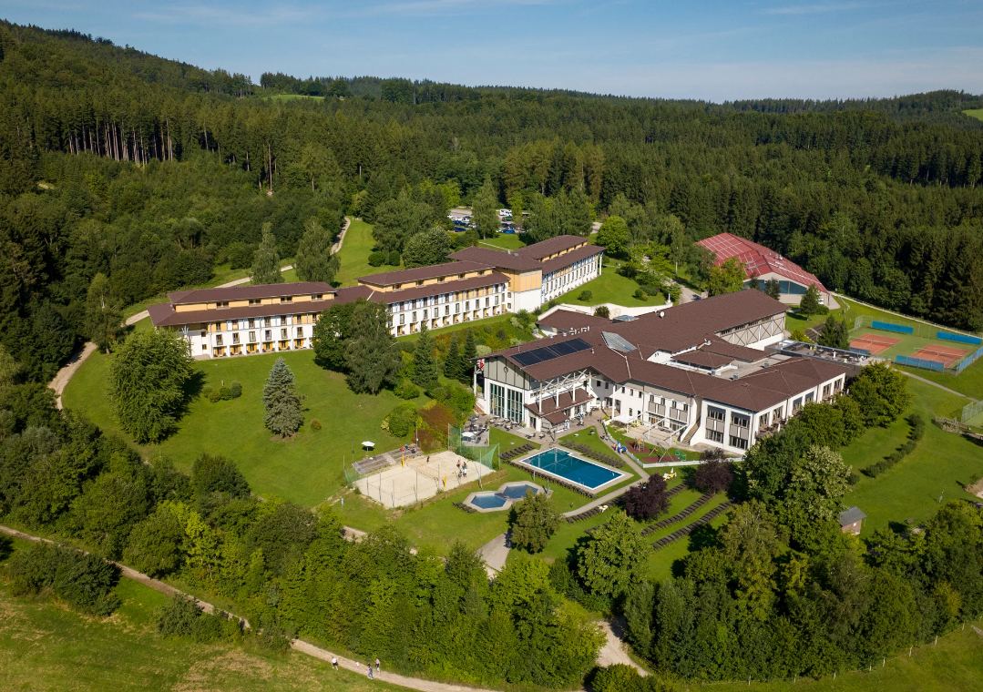 Aldiana Club Ampflwang aus der Luft: Hotelgebäude, Außenpool und Tennisplätze zwischen Wald und Wiesen