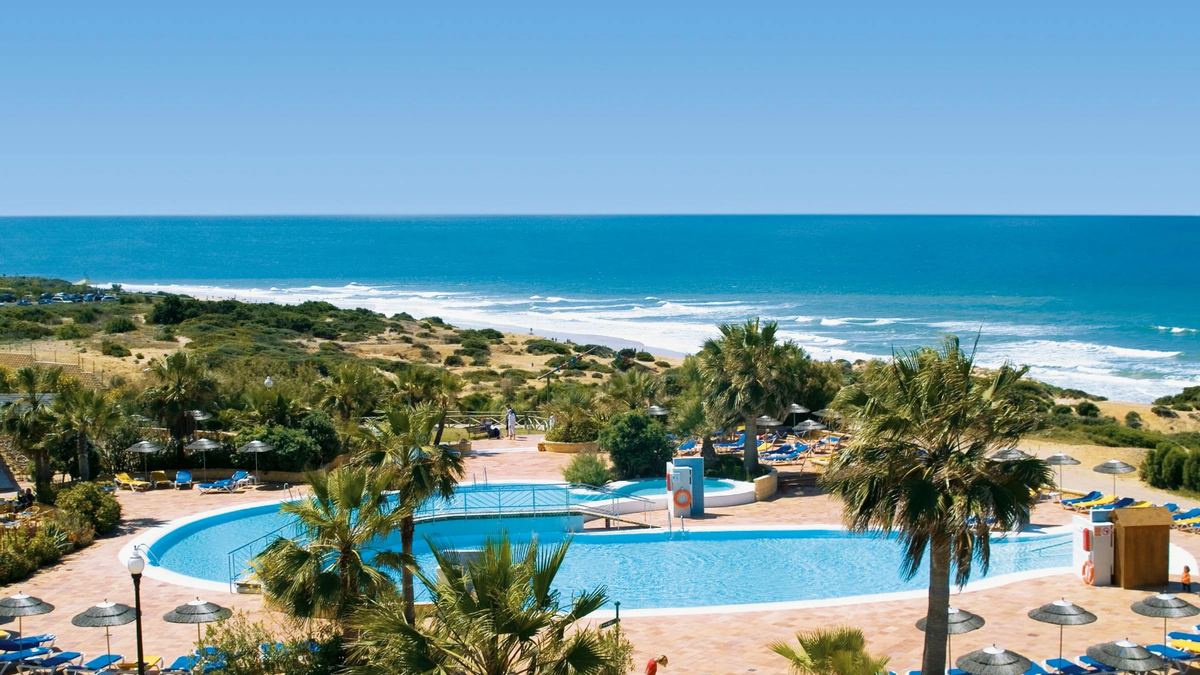 Pool mit Palmen im Aldiana Club Andalusien, dahinter Dünen, Strand und Atlantik