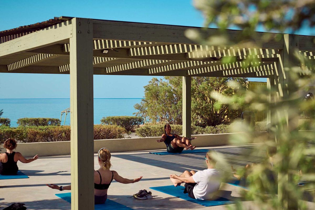 Kursgruppe auf Matten unter einer Holzpergola, im Hintergrund das Meer